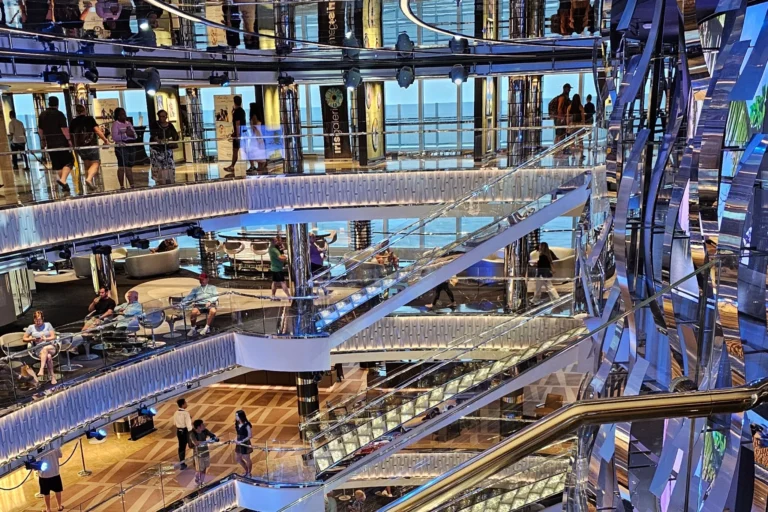 Mehrstöckiges Atrium der MSC Seashore mit gläsernen Treppen, spiegelnden Flächen und Passagieren an Bord