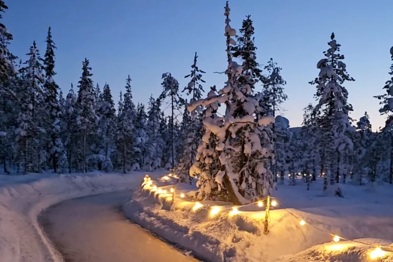 Beleuchteter Winterpfad beim Forest Ice Skating in Levi, Lappland mit verschneiten Bäumen in der Dämmerung