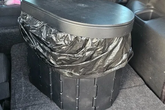 Faltbares Camping-Klo aufgebaut im Kofferraum eines Autos während eines Roadtrips.