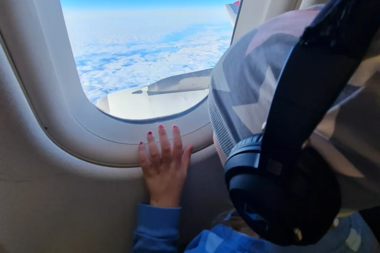 Kind im Flugzeug mit Kopfhörern am Fenster – entspannte Beschäftigung während des Flugs